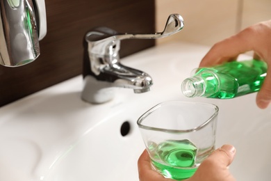 Man pouring mouthwash from bottle into glass in bathroom, closeup. Teeth care