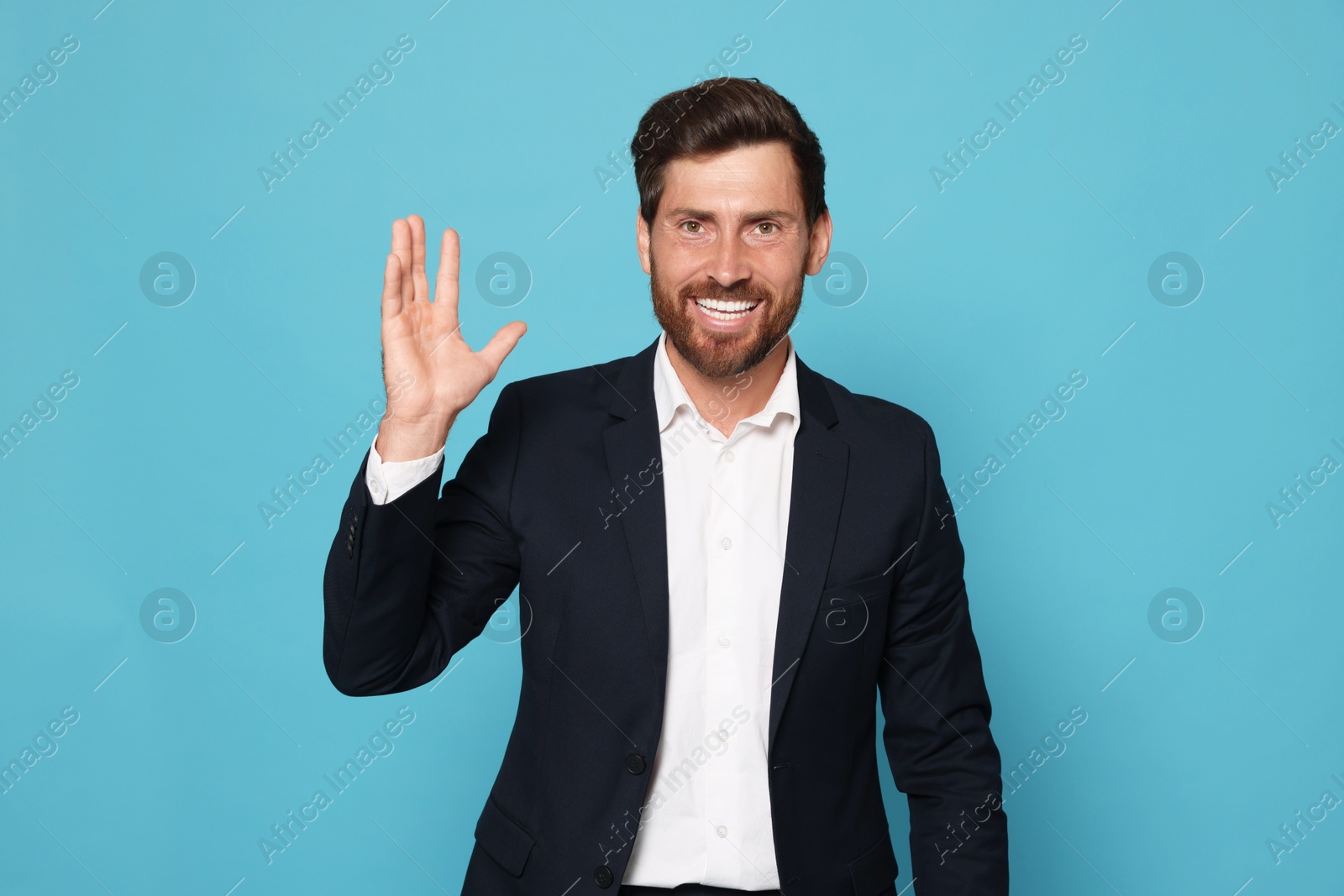 Photo of Smiling bearded man in suit showing hand on light blue background