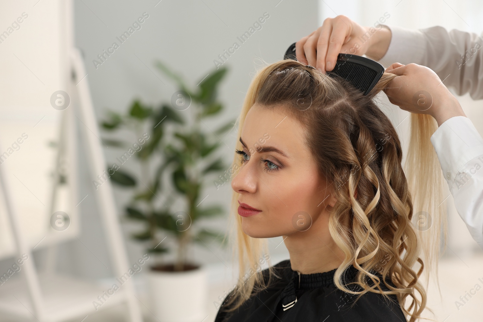 Photo of Hair styling. Hairdresser combing woman's hair in salon, closeup. Space for text