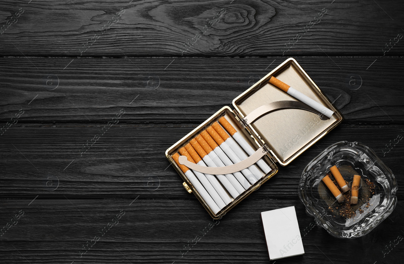 Photo of Cigarettes in case, matchbox and ashtray with stubs on black wooden table, flat lay. Space for text