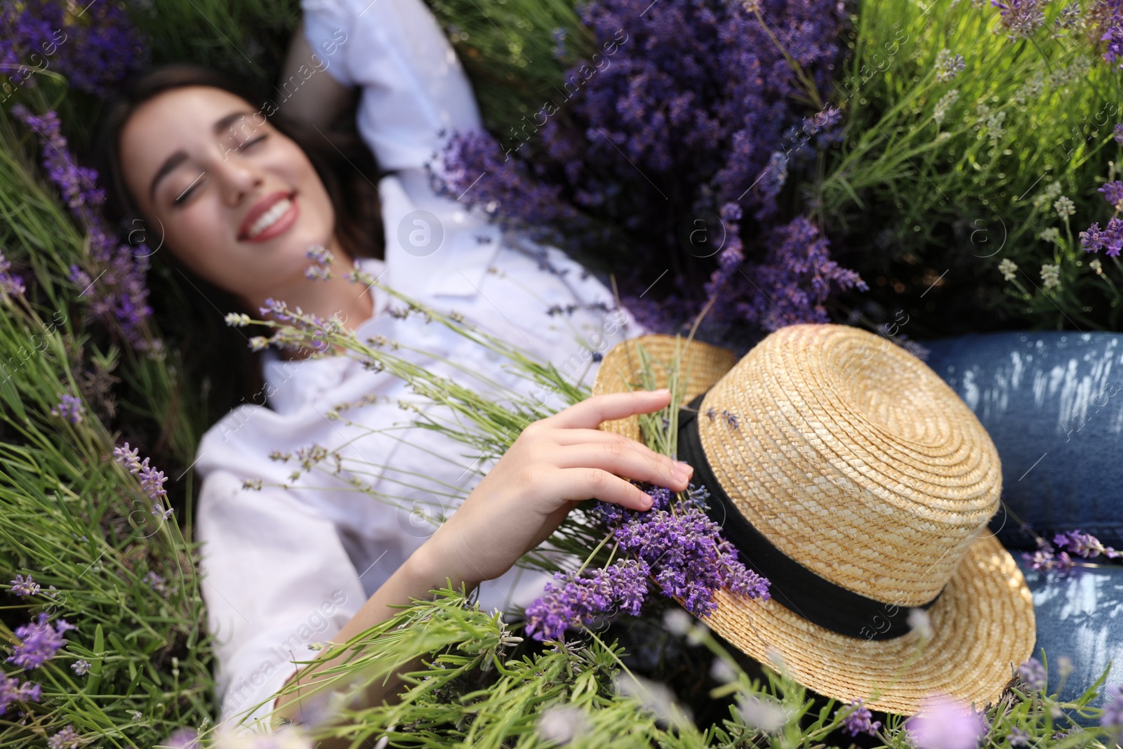 Photo of Young woman lying in lavender field on summer day, focus on hand with straw hat