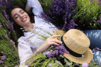 Young woman lying in lavender field on summer day, focus on hand with straw hat