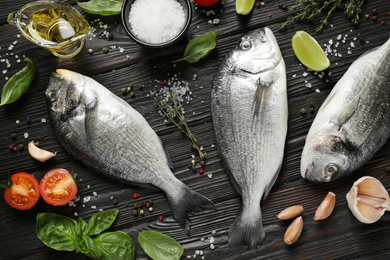 Flat lay composition with raw dorada fish on black wooden table