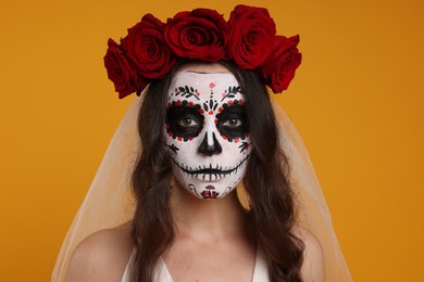 Photo of Young woman in scary bride costume with sugar skull makeup and flower crown on orange background. Halloween celebration