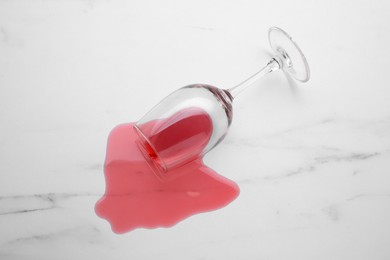 Photo of Glass with spilled red wine on white marble surface, top view