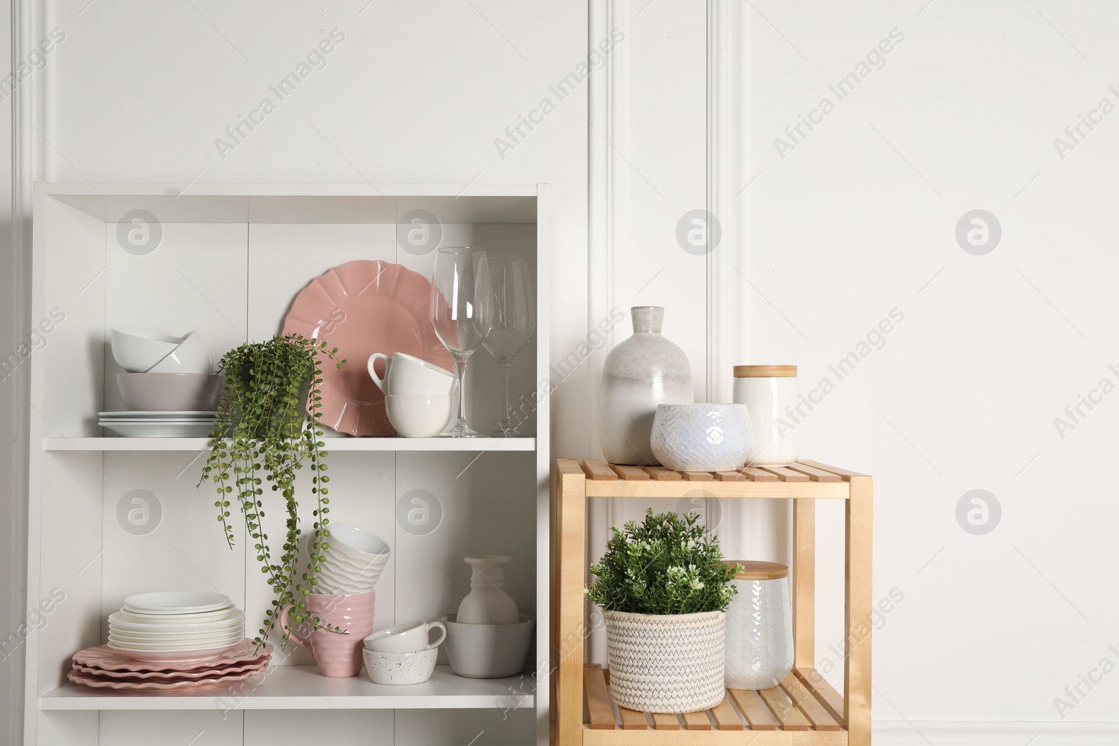 Photo of Different clean dishware and houseplants on shelves in cabinet indoors. Space for text