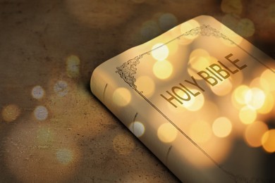 Image of Holy Bible on stone table, bokeh effect