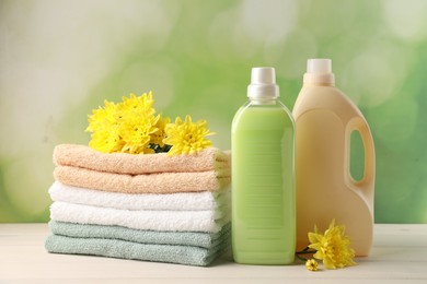 Photo of Bottles of laundry detergents, towels and beautiful flowers on white wooden table