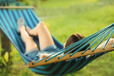 Young woman resting in comfortable hammock at green garden