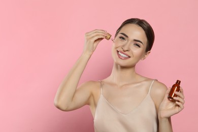 Photo of Young woman applying essential oil onto face on pink background, space for text