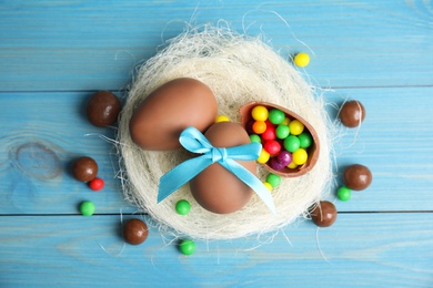 Photo of Flat lay composition with tasty chocolate eggs, colorful candies and decorative nest on light blue wooden table