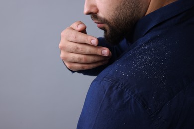 Photo of Man brushing dandruff off his shirt on grey background, closeup. Space for text