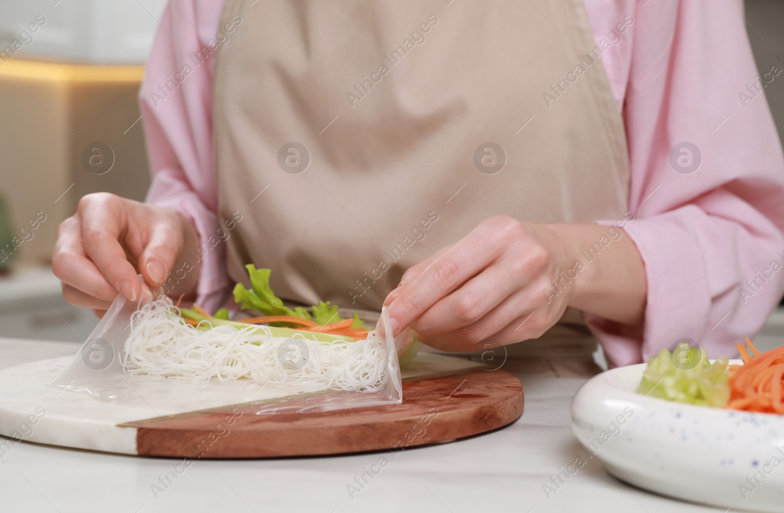 Photo of Making delicious spring rolls. Woman wrapping ingredients into rice paper at white table, closeup