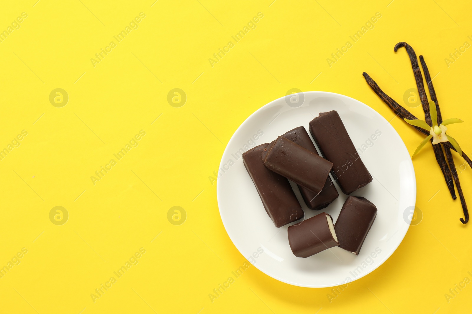 Photo of Glazed curd cheese bars, vanilla pods and flower on yellow background, top view. Space for text