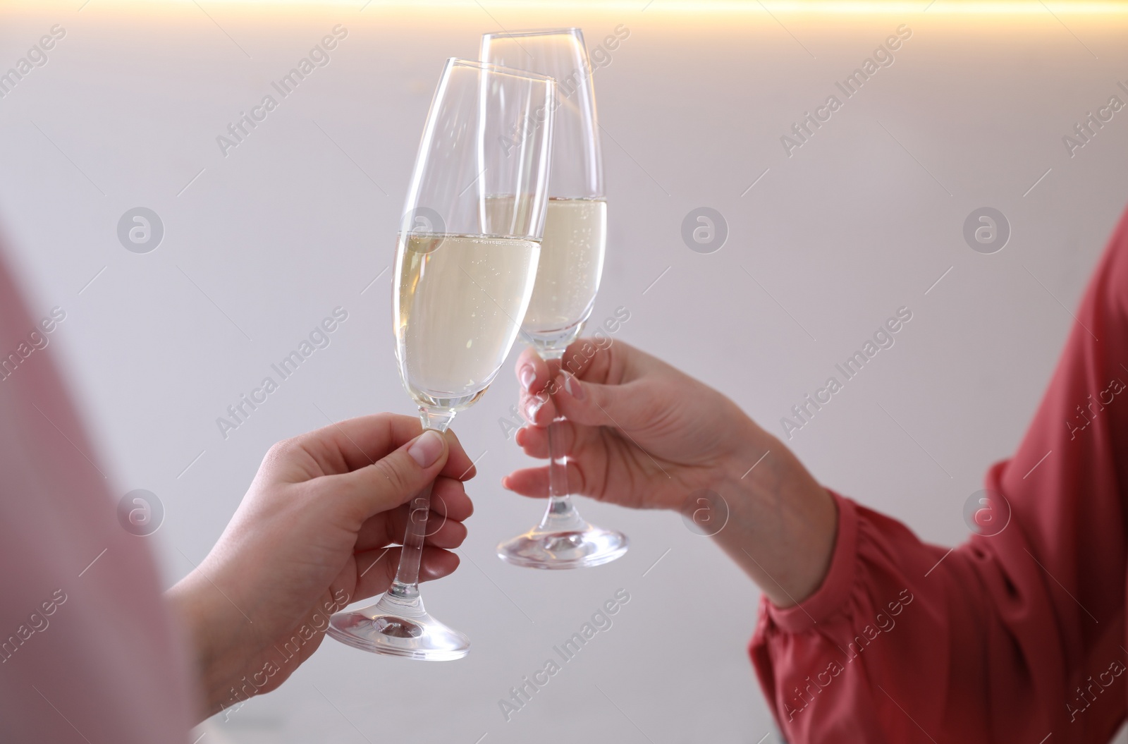 Photo of Women clinking glasses of champagne indoors, closeup. Holiday cheer and drink