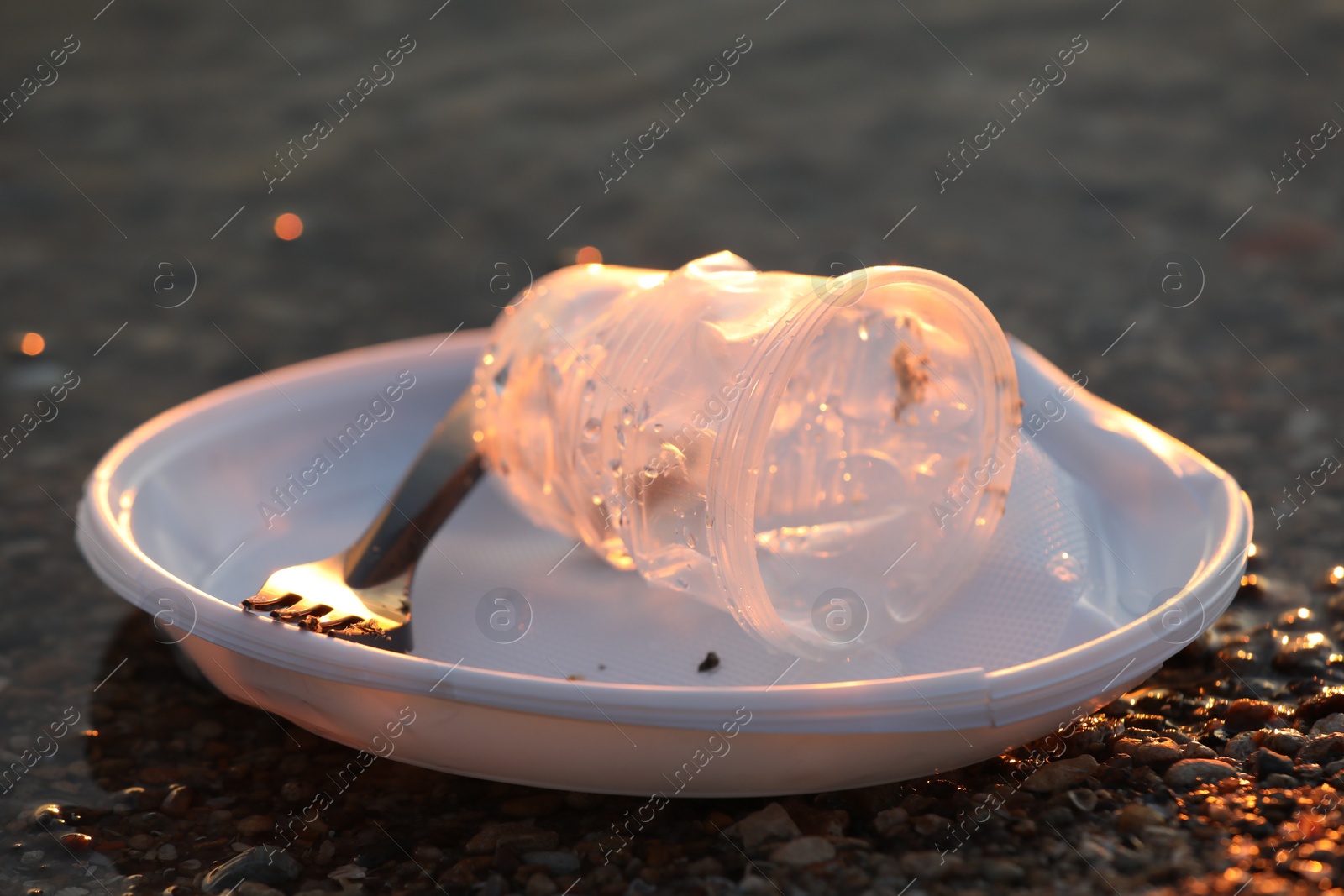 Photo of Used plastic tableware near water at beach, closeup. Environmental pollution concept