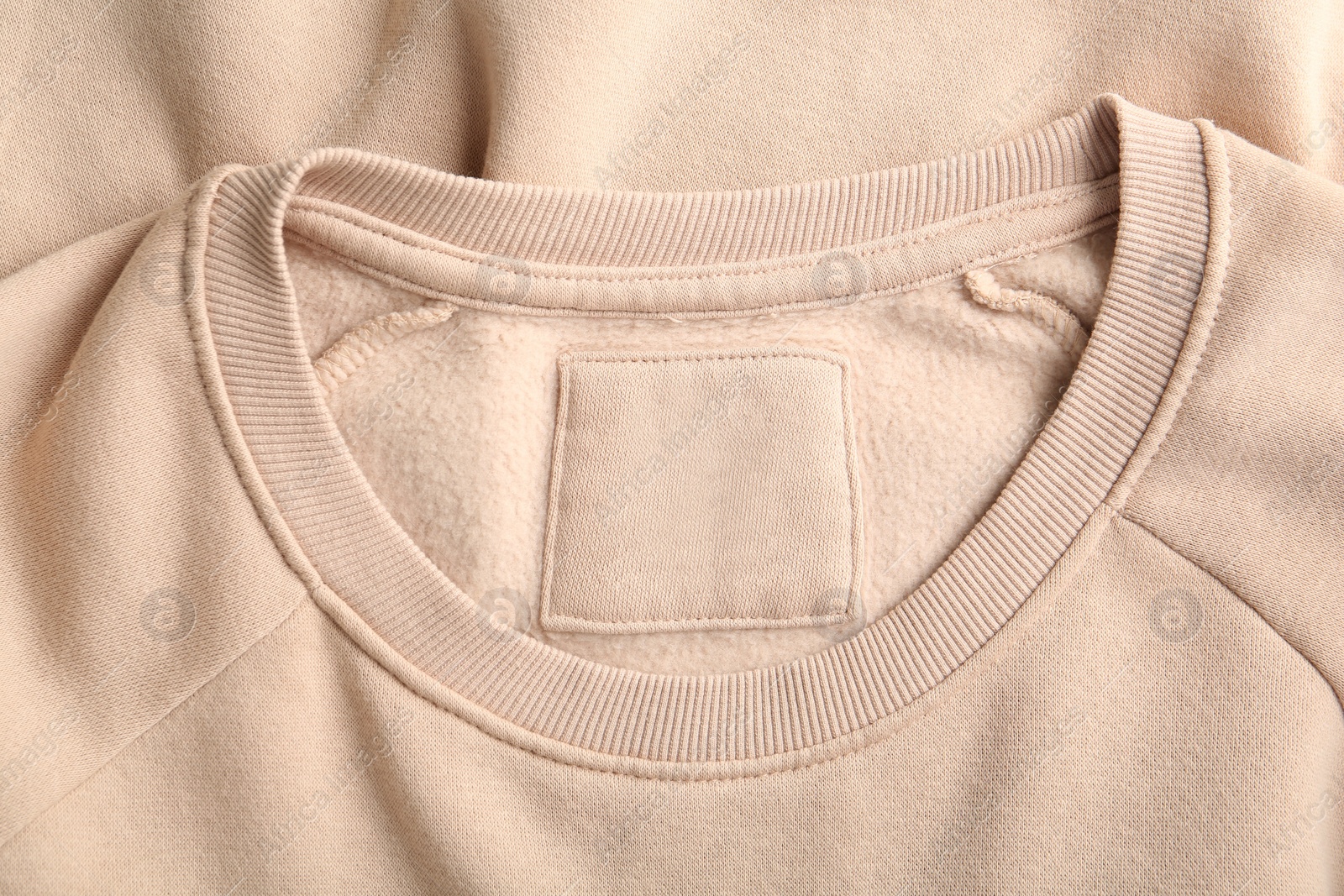 Photo of Blank clothing label on beige sweater, top view