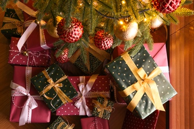 Photo of Pile of gift boxes near Christmas tree indoors, flat lay