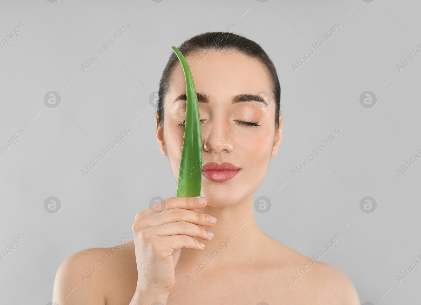 Photo of Young woman with aloe vera leaf on light grey background