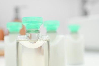 Mini bottles of cosmetic products on blurred background, closeup. Space for text