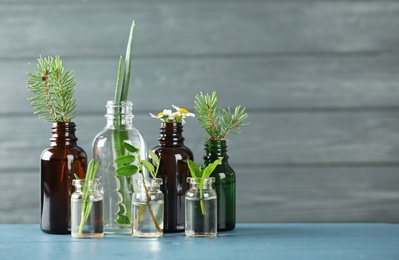 Photo of Glass bottles of different essential oils with plants on table. Space for text