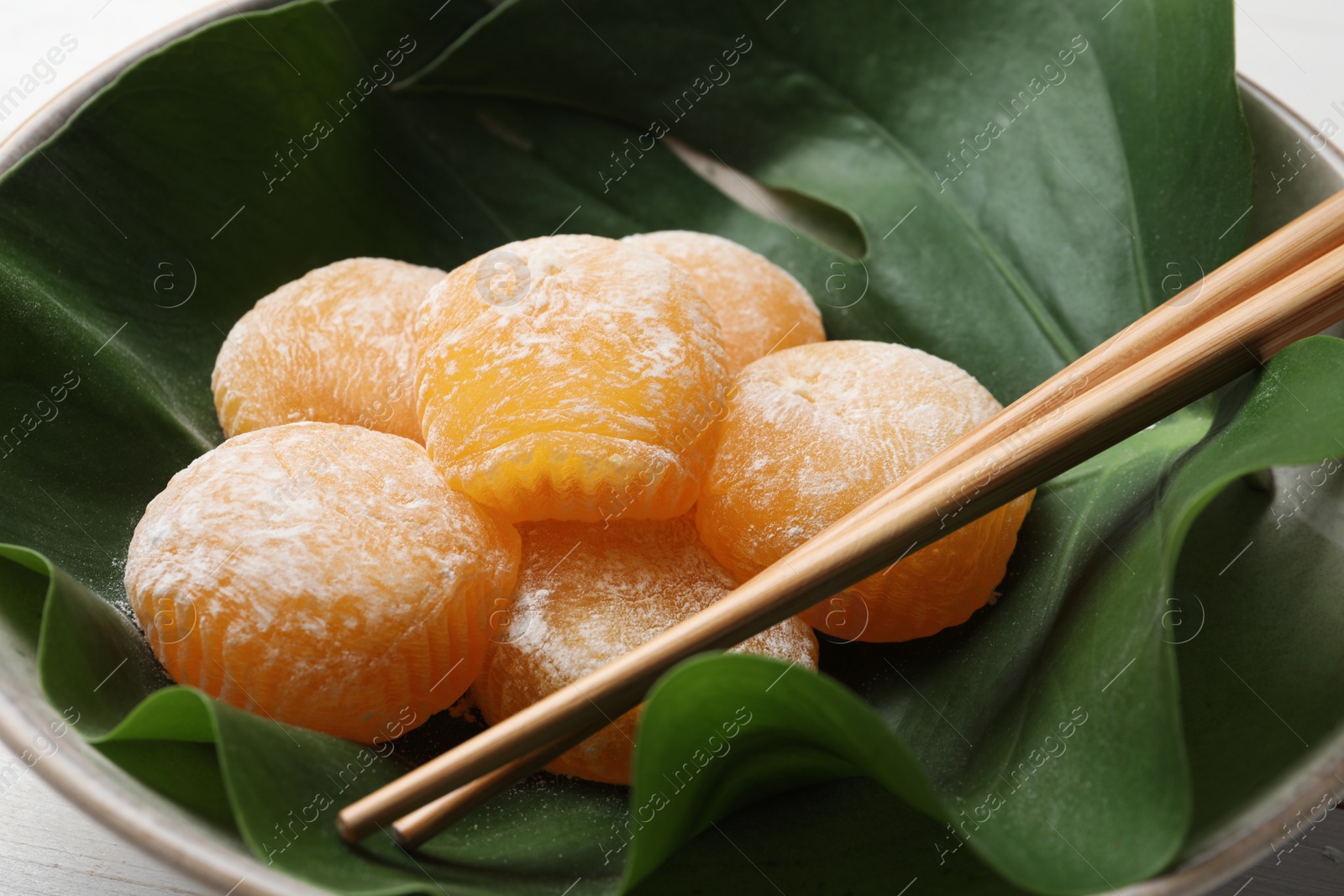 Photo of Delicious mochi served in bowl with green leaf and chopsticks on white table, closeup. Traditional Japanese dessert