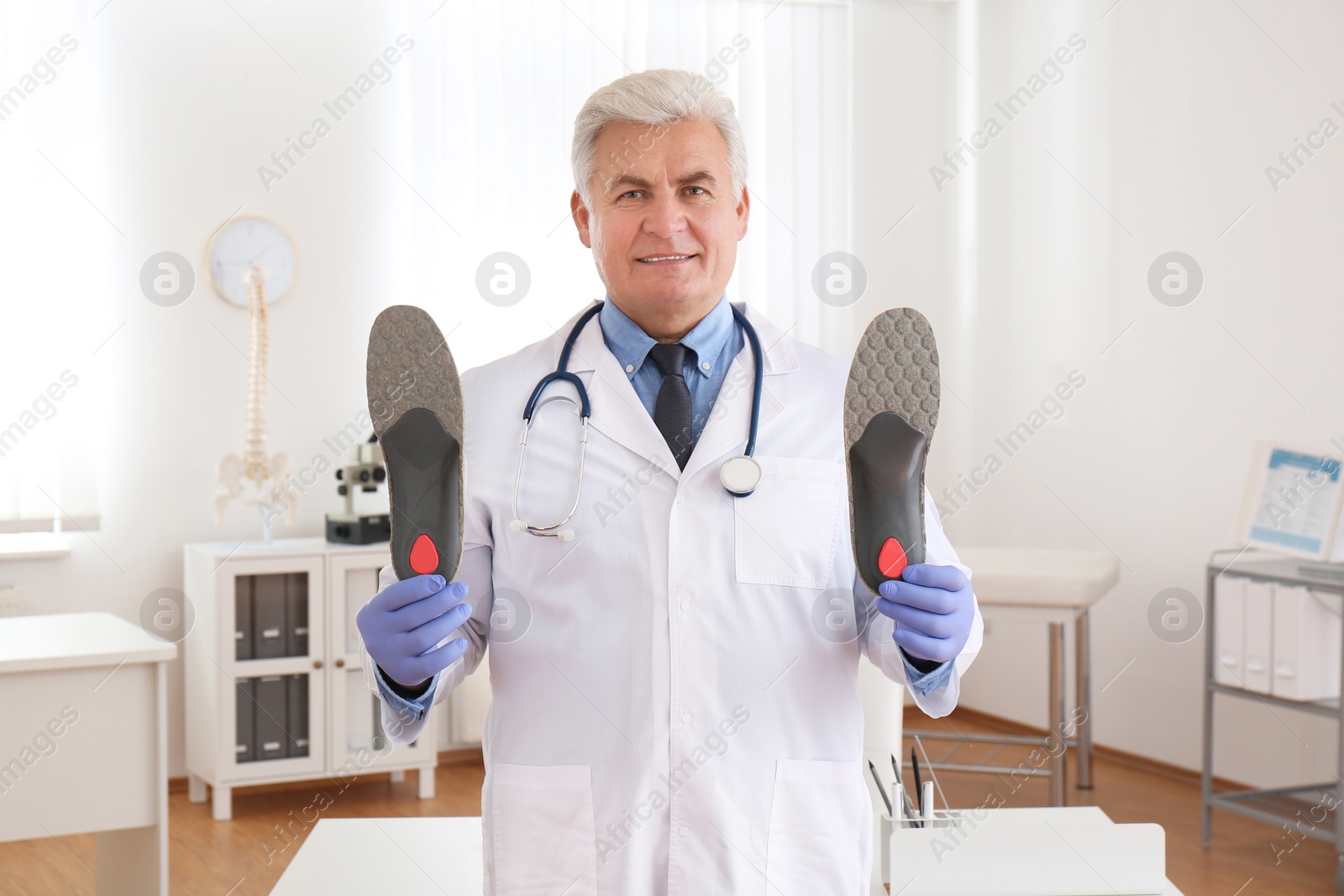 Photo of Senior male orthopedist showing insoles in clinic