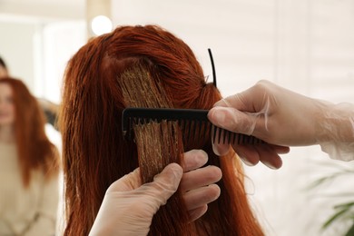 Photo of Professional hairdresser dyeing woman's hair with henna on blurred background, closeup