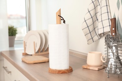 Photo of Roll of white paper towels and other kitchen stuff on wooden countertop indoors