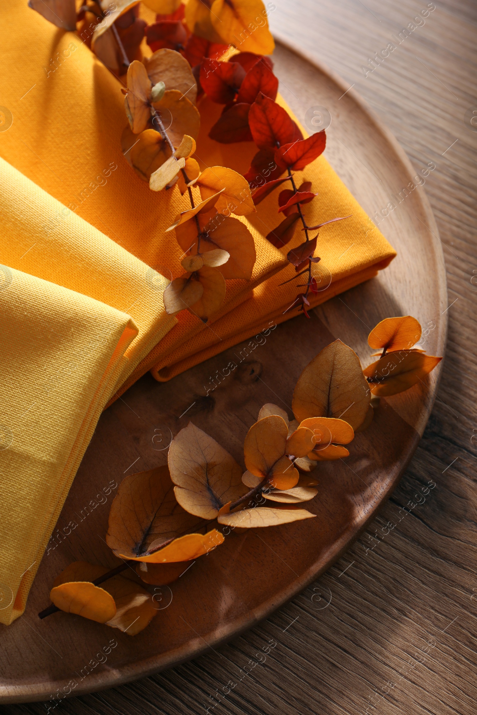 Photo of Tray with different kitchen napkins and decorative dry leaves on wooden table, top view