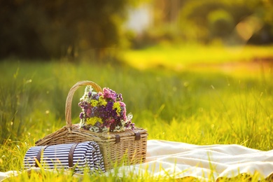 Photo of Picnic basket with wildflowers and mat on blanket outdoors. Space for text