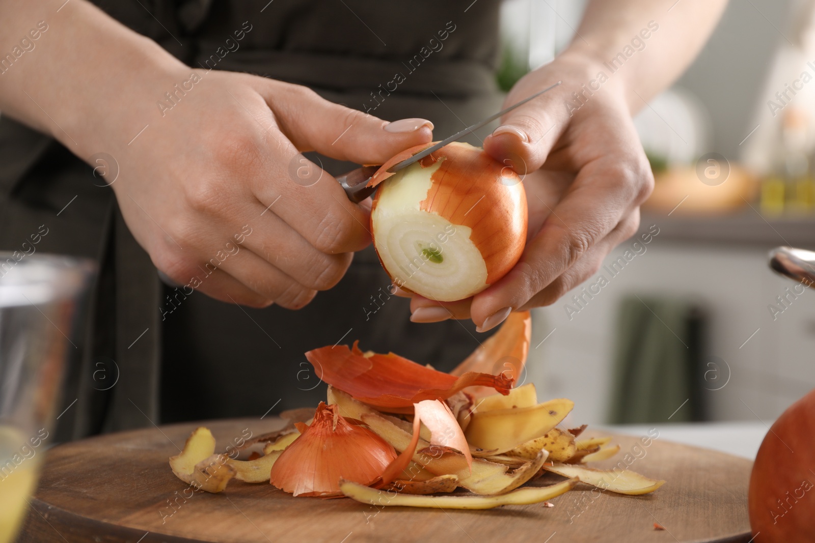 Photo of Woman peeling fresh onion with knife at table indoors, closeup