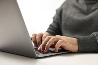 E-learning. Young man using laptop at white table, closeup