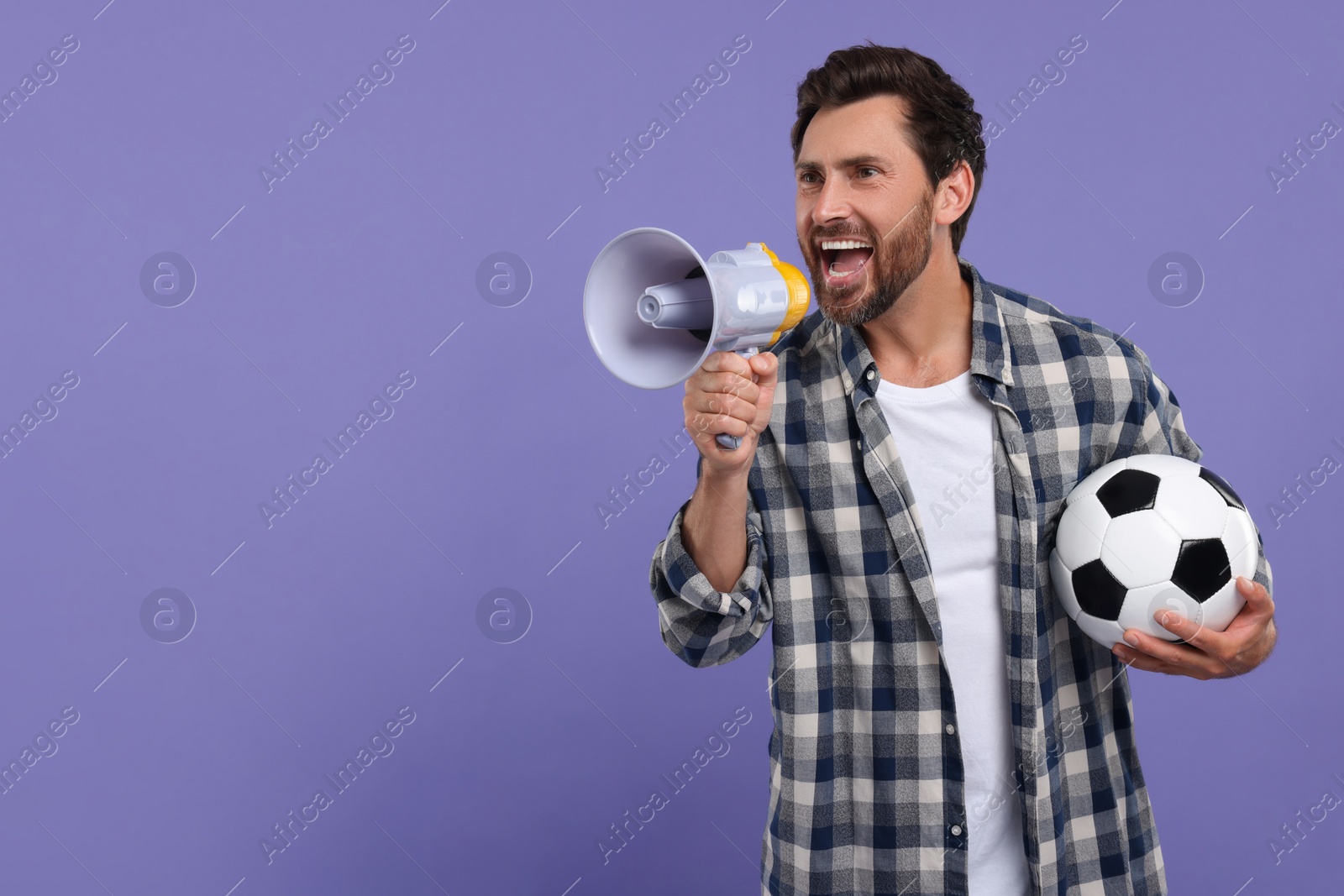 Photo of Emotional sports fan with soccer ball and megaphone on purple background, space for text