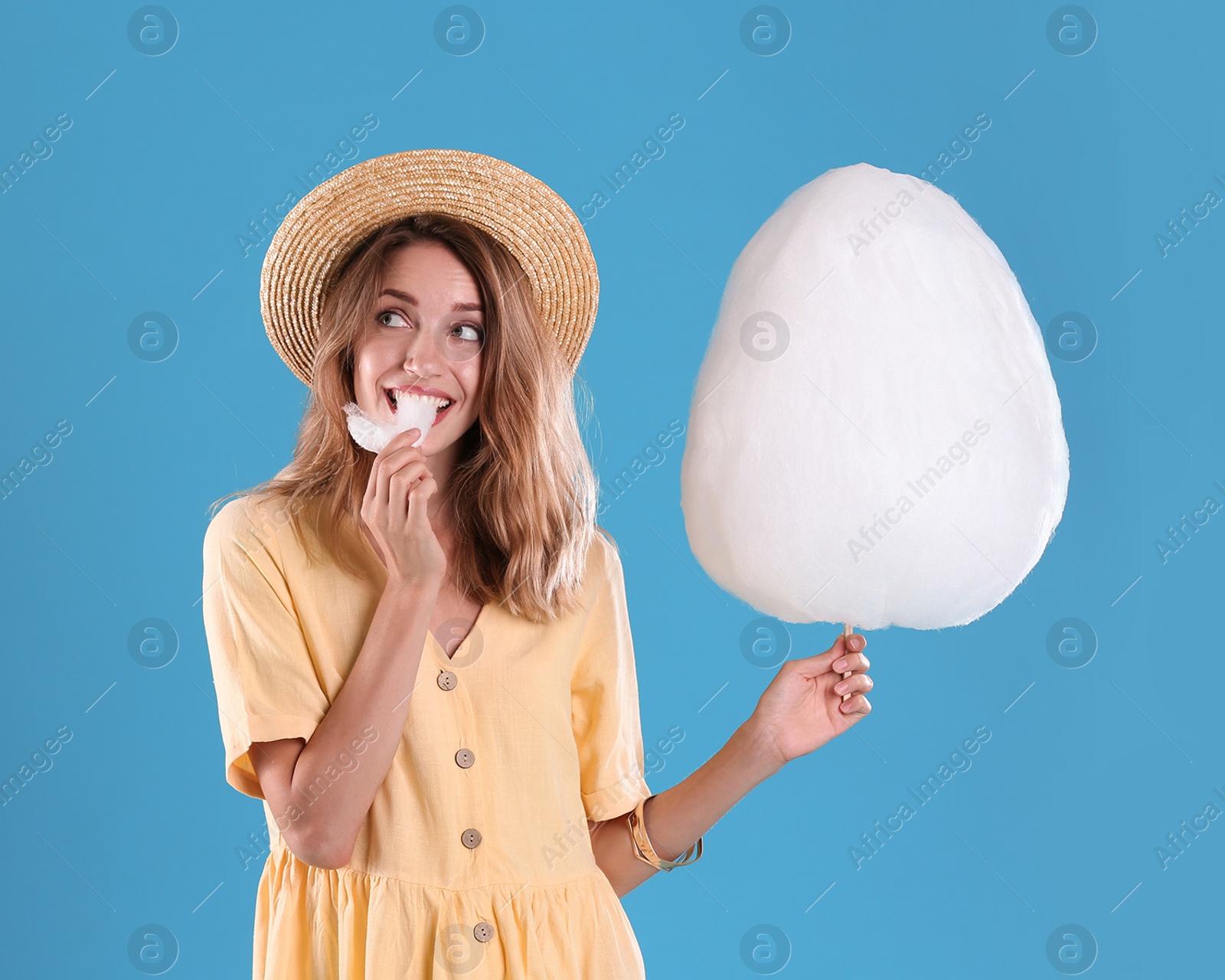 Photo of Happy young woman eating cotton candy on blue background