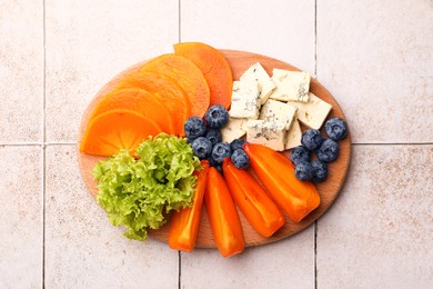 Photo of Delicious persimmon, blue cheese and blueberries on tiled surface, flat lay