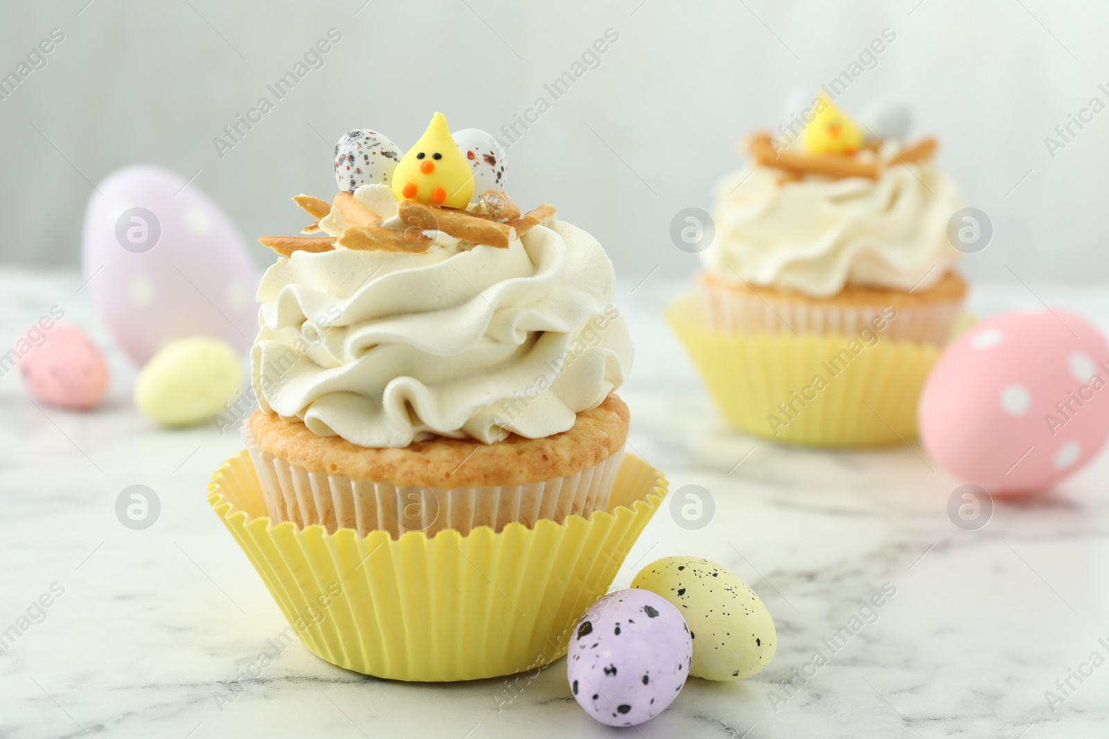 Photo of Tasty Easter cupcakes with vanilla cream and candies on white marble table