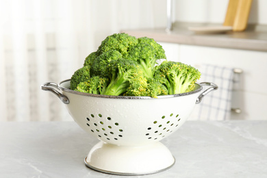 Photo of Raw green broccoli in colander on light grey marble table indoors