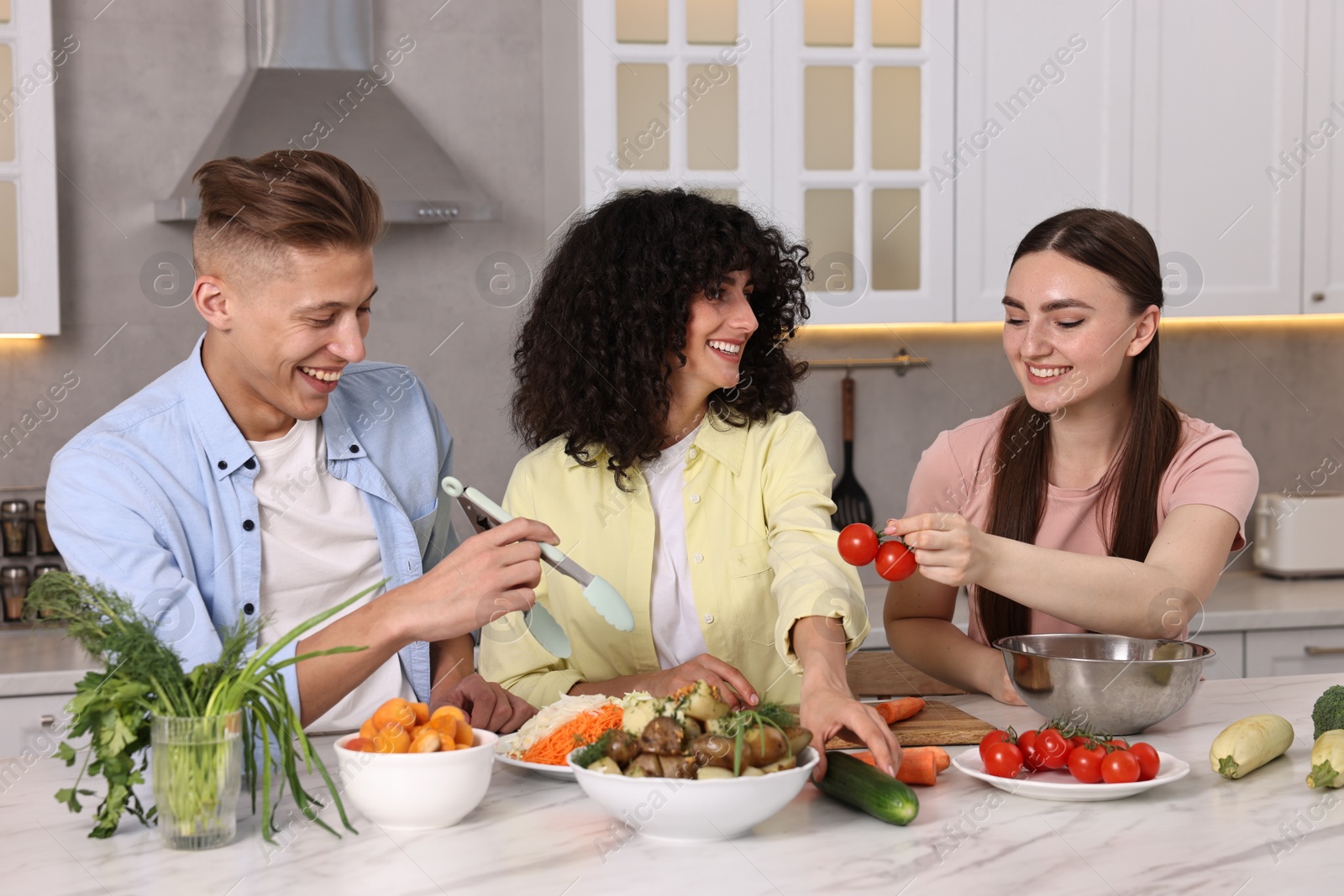 Photo of Friends cooking healthy vegetarian meal at white marble table in kitchen