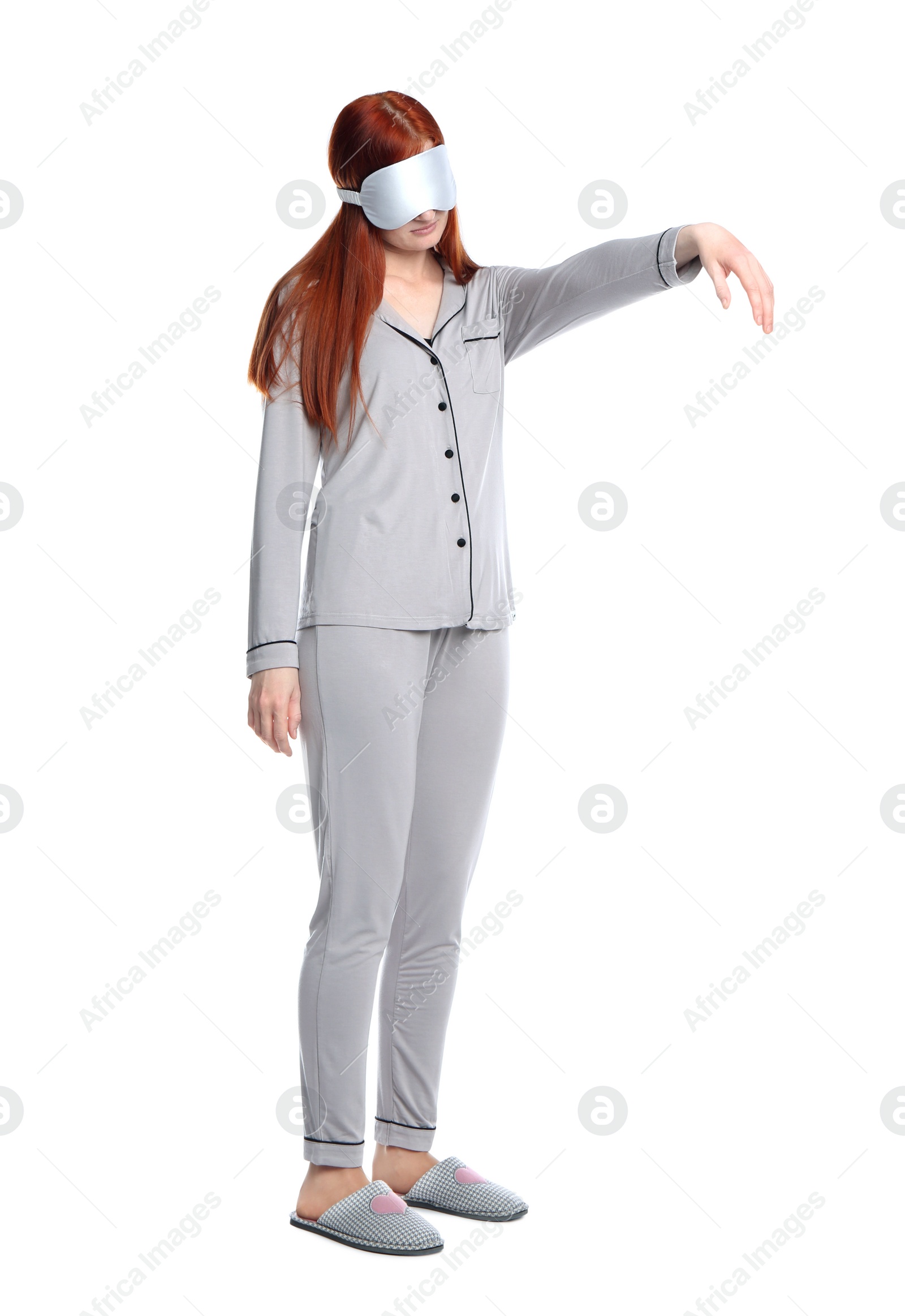 Photo of Young woman wearing pajamas, mask and slippers in sleepwalking state on white background