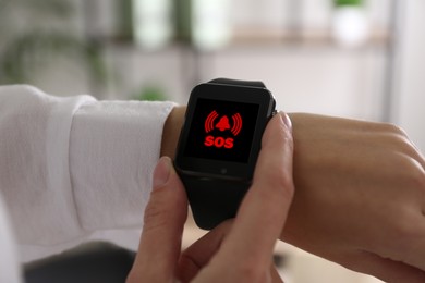 Woman using SOS function on smartwatch indoors, closeup