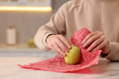 Man packing fresh apple into beeswax food wrap at light table in kitchen, closeup. Space for text