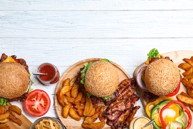 Photo of Flat lay composition with fresh bacon burgers and fries on white wooden table. Space for text