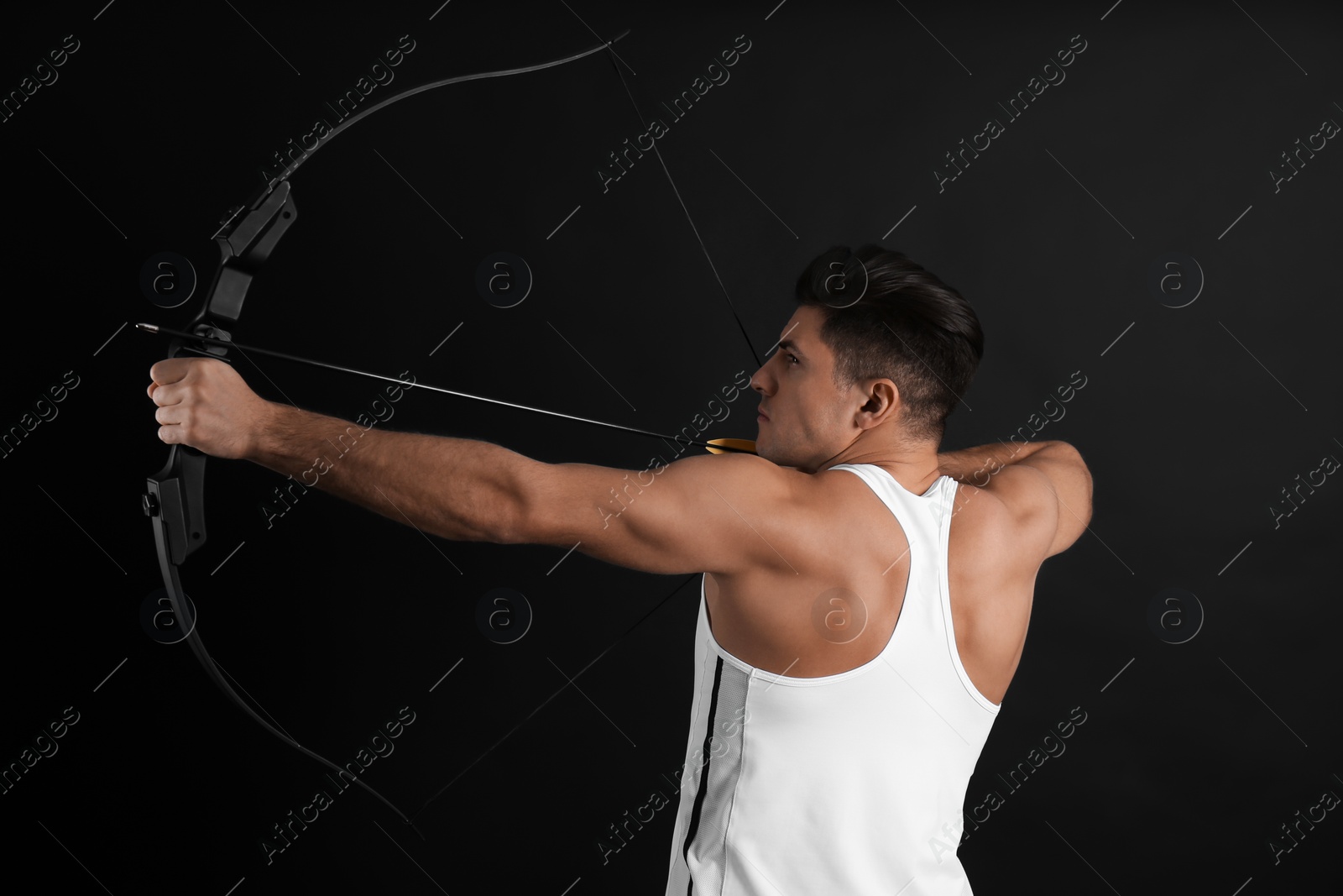 Photo of Man with bow and arrow practicing archery on black background