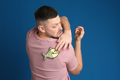 Photo of Man with paper fish on back against blue background. April fool's day