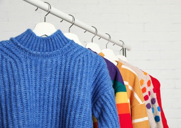 Photo of Collection of warm sweaters hanging on rack against white brick wall