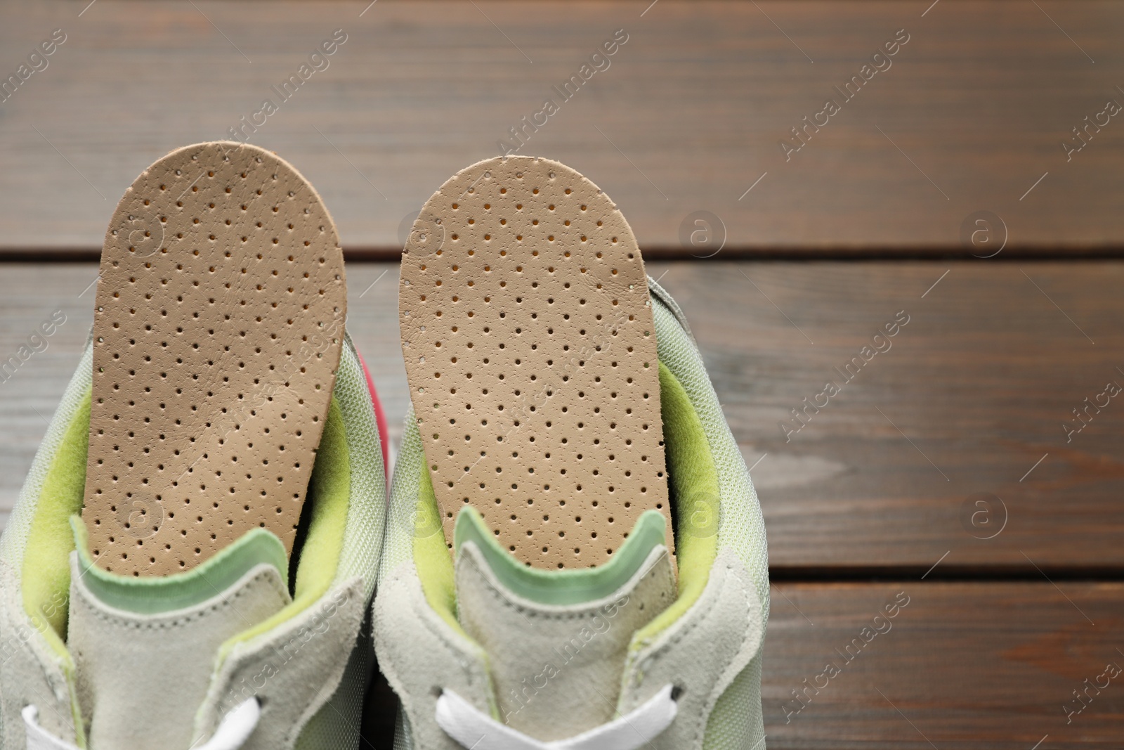 Photo of Orthopedic insoles in shoes on floor, closeup. Space for text