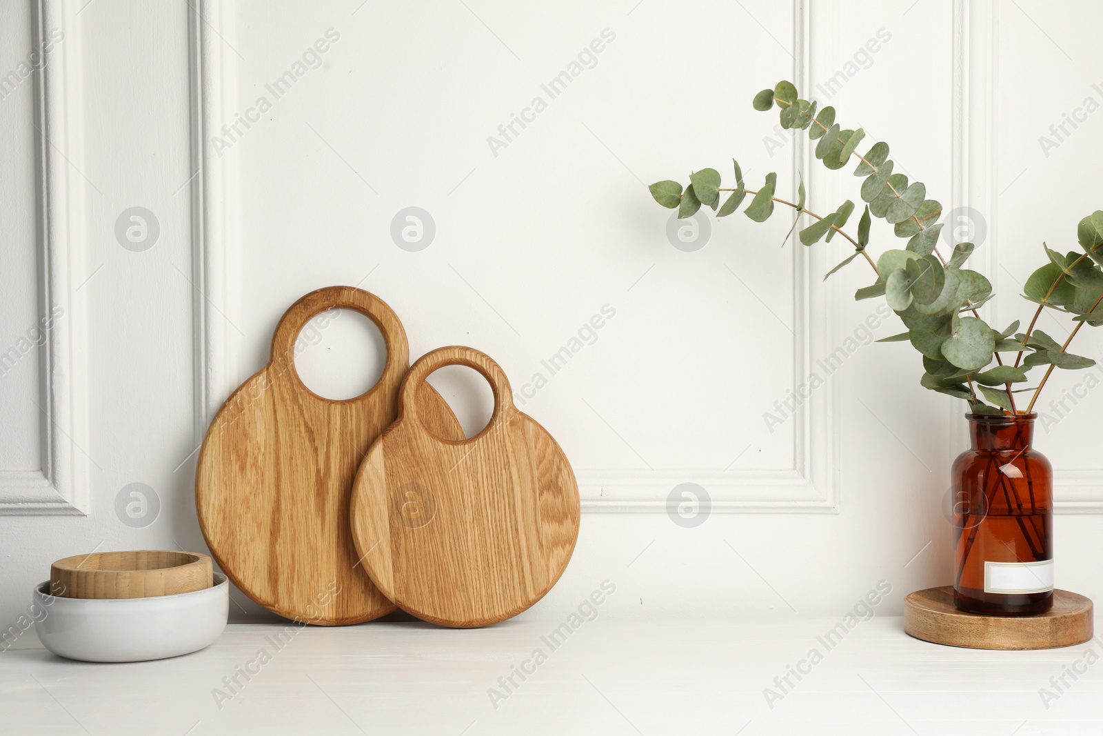 Photo of Wooden cutting boards, bowls and vase with eucalyptus branches on white table