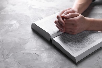 Religion. Christian woman praying over Bible at gray textured table, closeup. Space for text