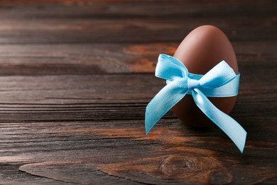 Photo of Tasty chocolate egg with light blue bow on wooden table, space for text